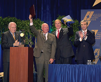 Photo showing Vice President Dick Cheney and Commerce Secretary Carlos Gutierrez presenting the 2005 Baldrige National Quality Award to representatives of DynMcDermott Petroleum Operations Company. Since 1993, the firm has operated and maintained the U.S. Strategic Oil Reserve, a cache of up to 700 million barrels of crude oil.